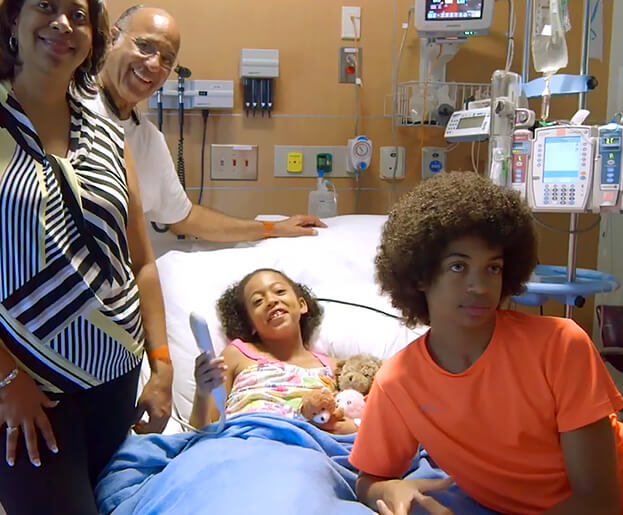 A family gathered around a child in a hospital room watching Wildlife Explorers programming
